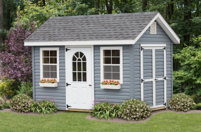 a frame shed with blue siding, white windows and doors, flower boxes, and shrubs along the perimeter