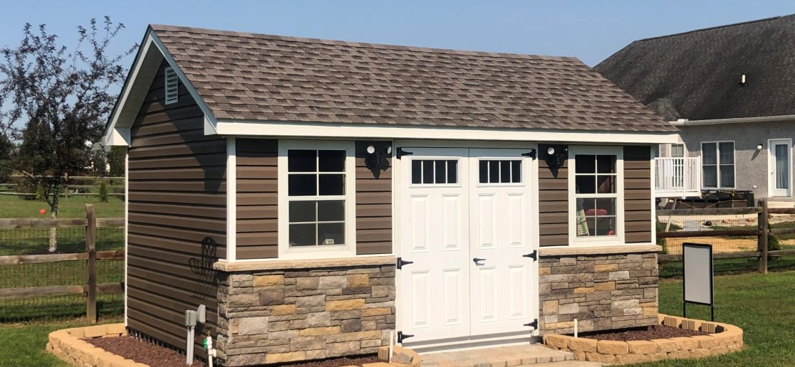 classic garden cottage with brown siding, stone features, white double doors, and a stone perimeter