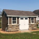 classic garden cottage with brown siding, stone features, white double doors, and a stone perimeter