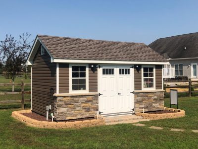 classic garden cottage with brown siding, stone features, white double doors, and a stone perimeter