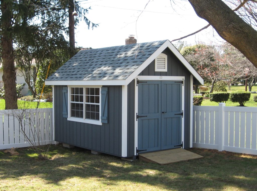 classic garden cottage shed with blue siding, white trim, and paving slab shed pad