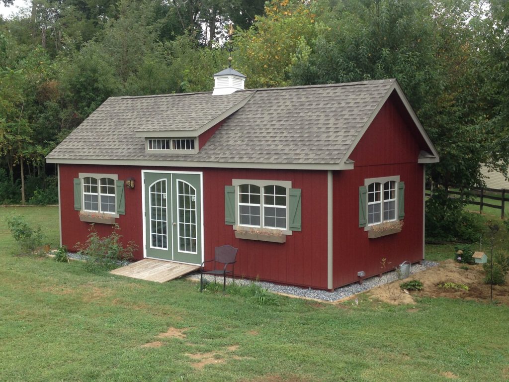 dormer shed with red siding, ramp, cupola, and green doors and shutters