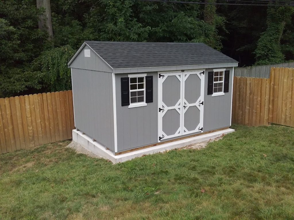 standard cottage shed with gray siding, black shutters, and concrete shed pad