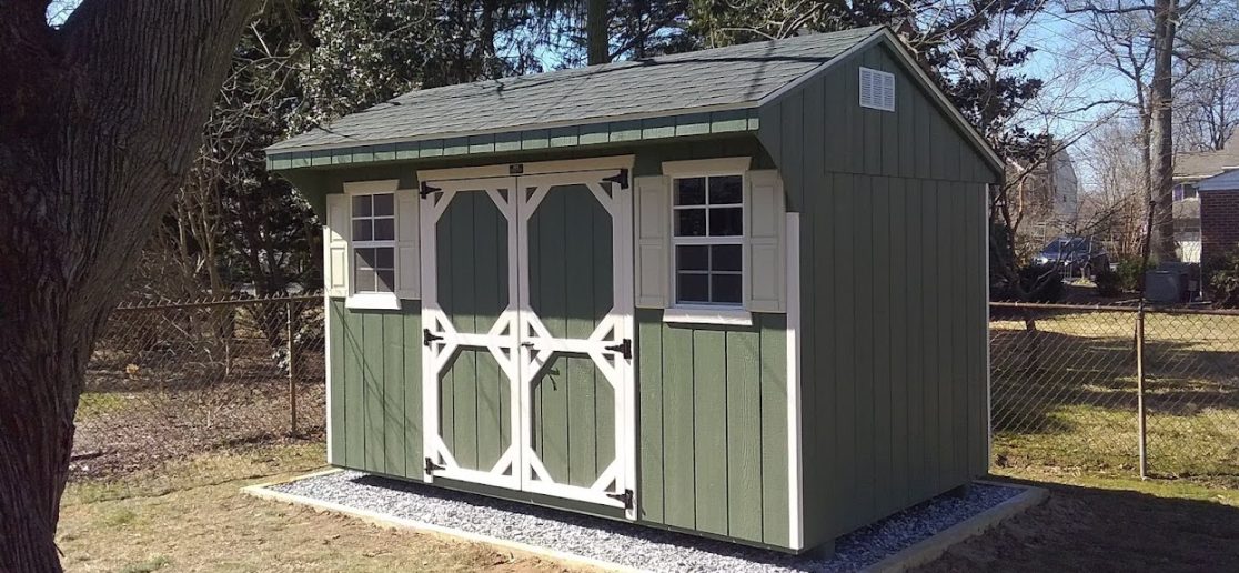 quaker shed with green siding and white trim, crushed stone shed pad