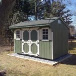 quaker shed with green siding and white trim, crushed stone shed pad