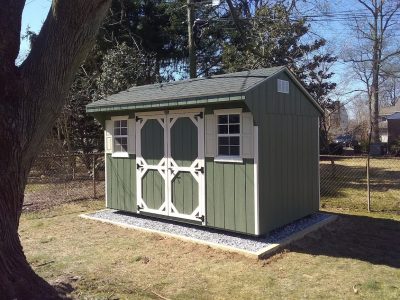 quaker shed with green siding and white trim, crushed stone shed pad